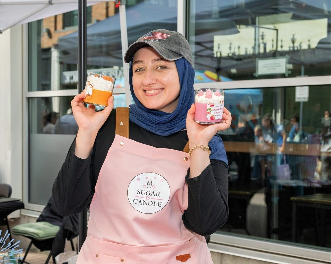 Person in a pink apron holding small containers at an outdoor event with 'Riverfest at Assembly Row' branding.