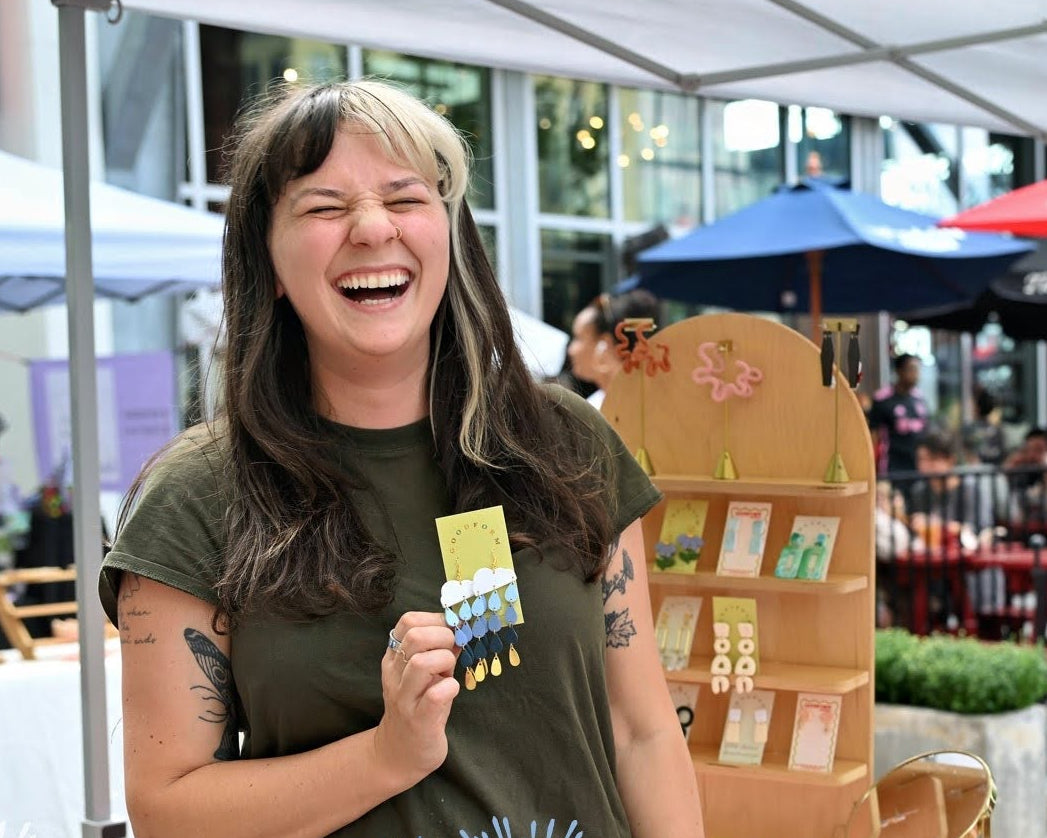 Woman at an outdoor market event holding a product, with 'Riverfest at Assembly Row' branding.