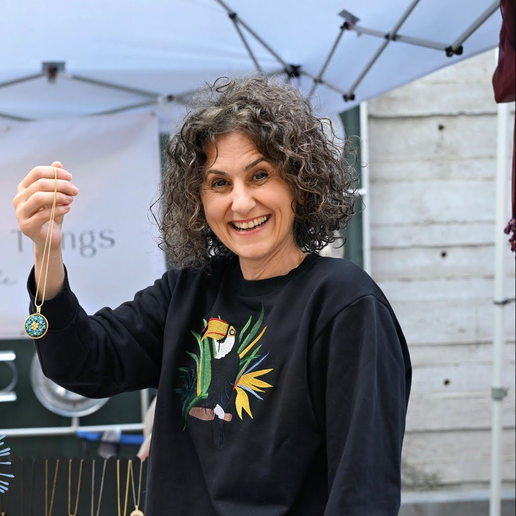 Person holding a small object in front of a 'Teeny Weeny Things' booth at Riverfest at Assembly Row.