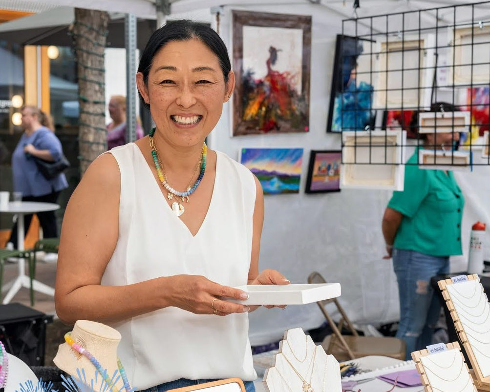 Woman at an outdoor market stall with 'Riverfest at Assembly Row' branding.