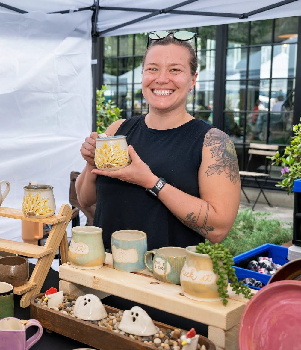 Woman holding a ceramic mug at a Riverfest event at Assembly Row with various ceramic items displayed.
