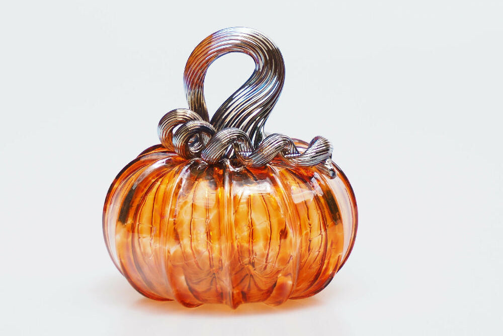 An orange glass pumpkin figurine with a twisted metallic silver stem, set against a plain white background.