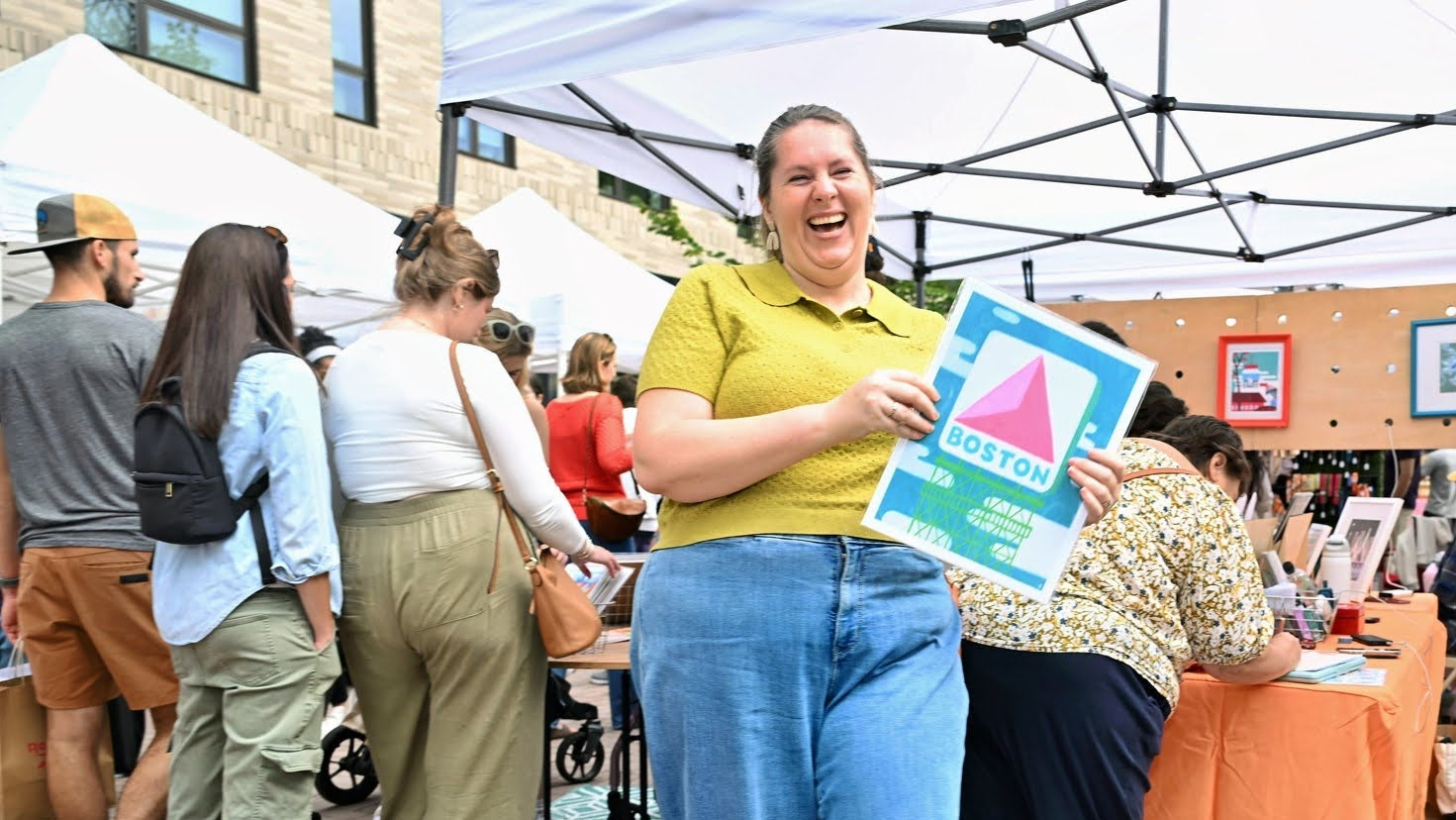 Woman holding a colorful sign at an outdoor event with 'Riverfest at Assembly Row' branding.