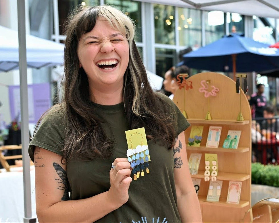 Woman at an outdoor market event holding a product, with 'Riverfest at Assembly Row' branding.